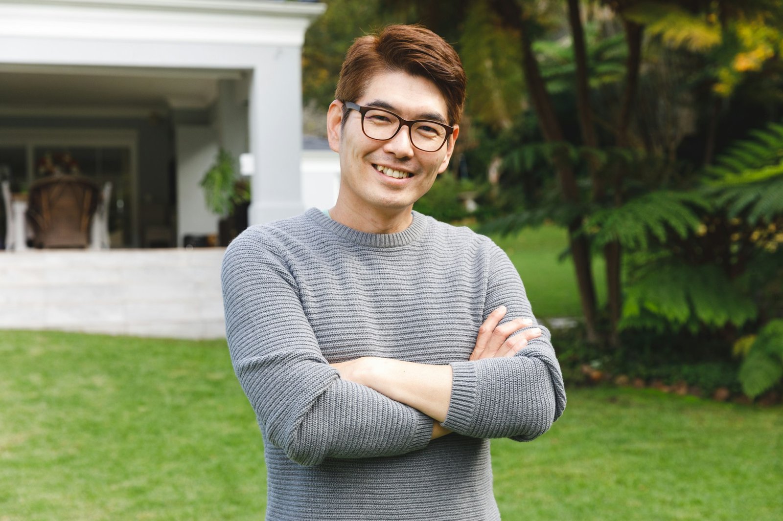 Portrait of happy asian man wearing glasses smiling in garden outside family home